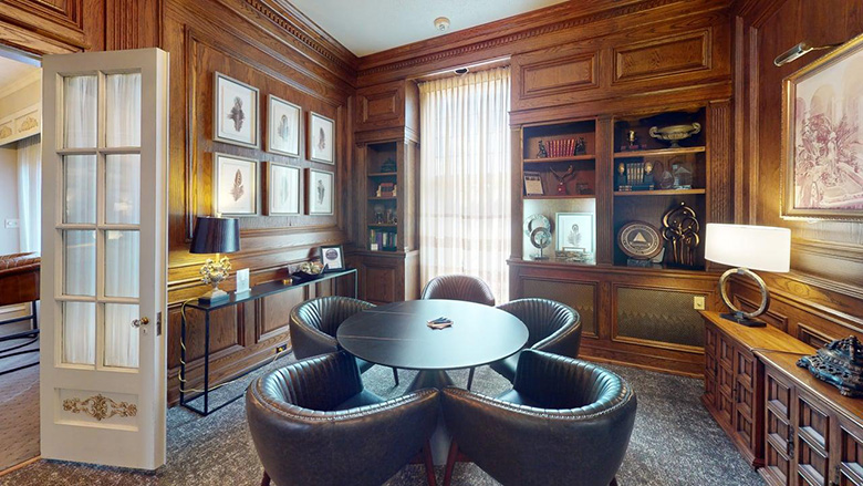 Elegant office with wood-paneled walls, a round table with four leather chairs, built-in bookshelves, framed art, and a console table with decorative items—perfect for sophisticated meetings at Dunn's Chapel, with sheer curtains welcoming natural light.