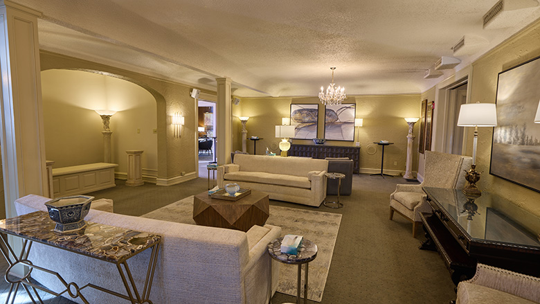 A spacious, elegant living room in Dunn's Chapel with beige sofas, a large rug, a wooden coffee table, decorative lamps, wall art, and a chandelier. The warm lighting creates a cozy and inviting atmosphere.