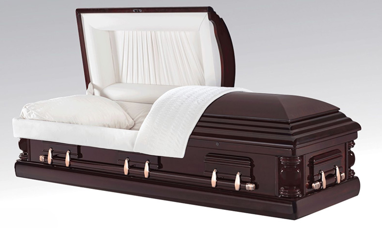 A polished dark wood casket, a type of burial merchandise, with a white interior lining and pillow is shown partially open, revealing its cushioned inside. The background is plain and light gray.