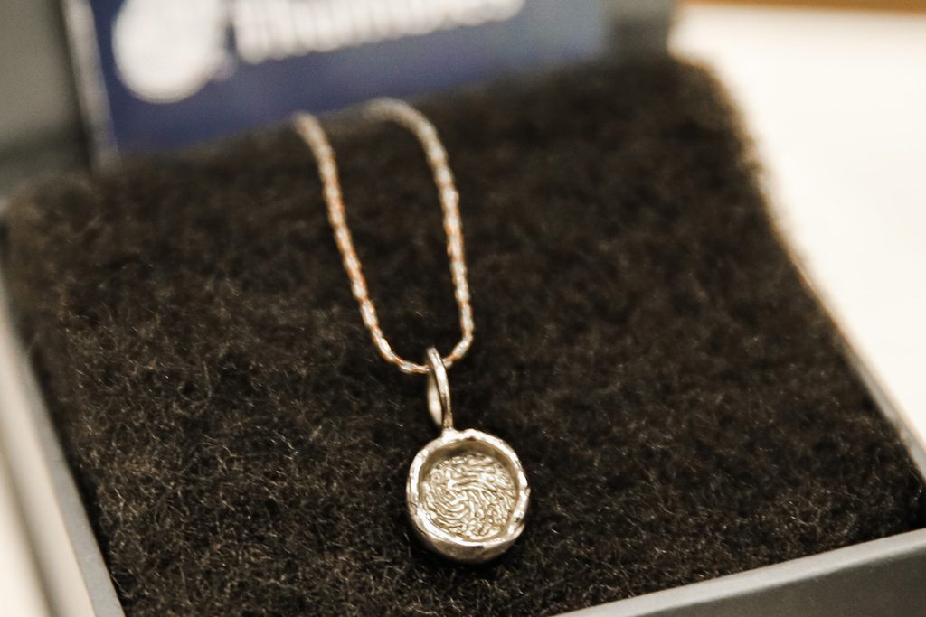 A silver necklace with a round, textured pendant displayed on a black, fuzzy jewelry box lining—an elegant keepsake often included in select cremation packages.