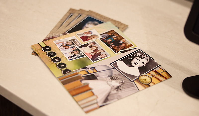 A close-up of a collage featuring vintage and family photos, laid out on a white surface, with glimpses of life celebrations and postcards partially visible beneath it.