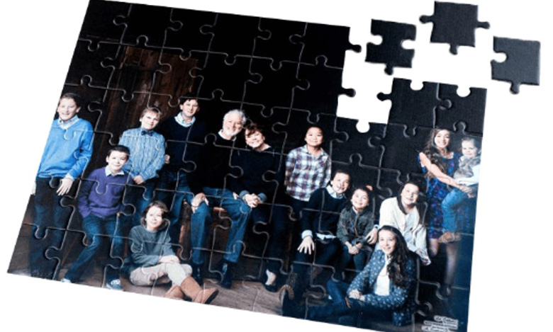 A partially completed jigsaw puzzle shows a family portrait with adults and children posing together, capturing the essence of life celebrations; a few puzzle pieces are missing from the top right corner.