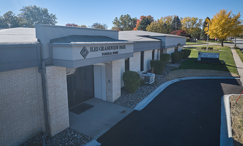 A single-story building with a sign reading “ILES GRANDVIEW PARK FUNERAL HOME” above the entrance, Iles Grandview Park Chapel is surrounded by landscaping, a paved driveway, and autumn trees in the background.