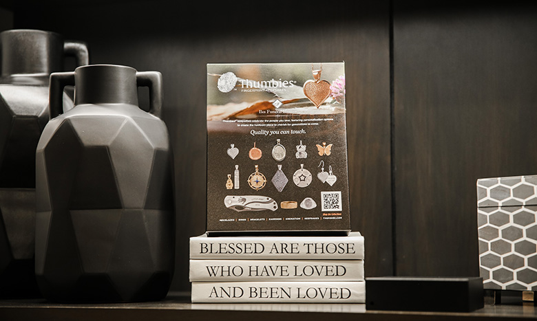 A decorative shelf displays black vases, a geometric-patterned box, and three stacked books titled BLESSED ARE THOSE WHO HAVE LOVED AND BEEN LOVED, with a small sign featuring jewelry and keepsakes from Jordan Creek Chapel on top.